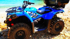 Un cuatrimoto azul con un compartimento de almacenamiento en una playa rocosa.