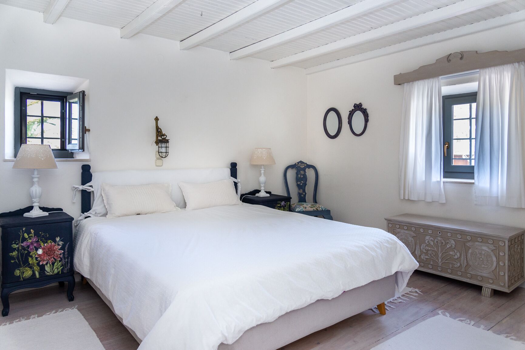 A bedroom with a large bed, two bedside tables with lamps, a dresser, and a window with curtains.