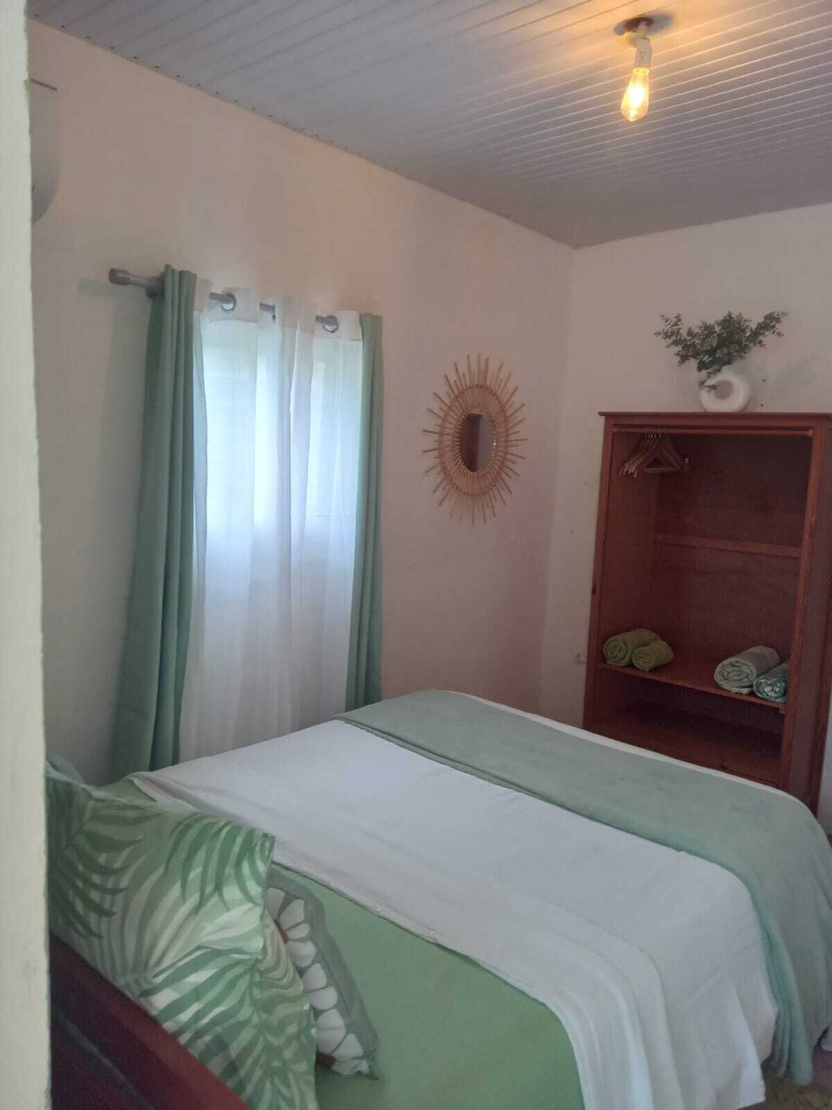 Une petite chambre à coucher, bien rangée, avec un lit simple, une armoire en bois et un ventilateur de plafond.