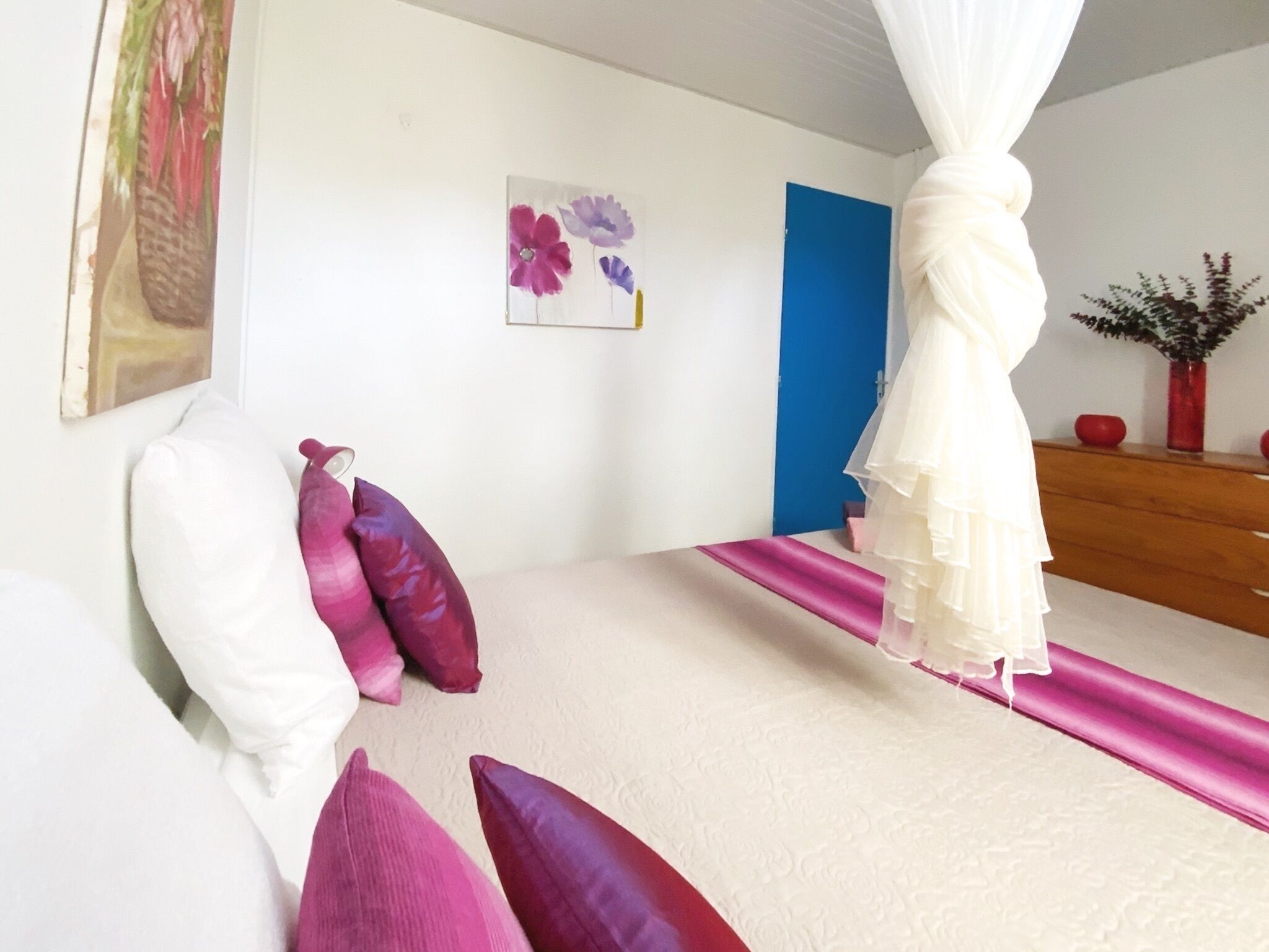 A bedroom with a bed, pillows, a bedside table, a nightstand, a wall art, a door, and a curtain.
