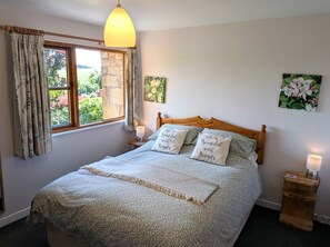 A bedroom with a bed, a nightstand, a lamp, a window with curtains, and a painting on the wall.