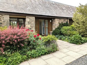 A stone building with a tiled roof, a wooden door, and a paved pathway leading to the entrance.