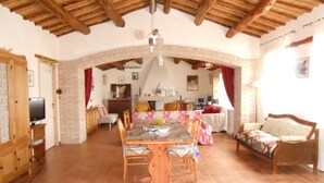 A spacious dining area with a wooden table and chairs, a kitchen in the background, and a cozy living area with a sofa and a TV.