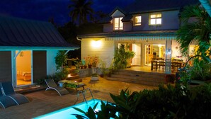 A house with a swimming pool, outdoor seating, and a well-lit patio area.