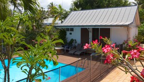 Un espace aménagé au bord de la piscine, comprenant une piscine, des chaises longues et un petit bâtiment doté d’un toit en pente.