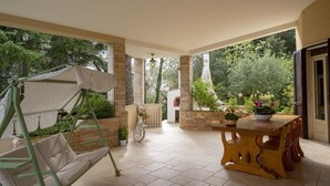 A covered patio area with a swing chair, a table with potted plants, and a bicycle.