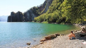 Un rivage rocheux bordé d’une eau claire, et une personne assise sur la plage.
