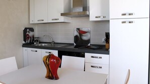 Une cuisine moderne avec des armoires blanches, une hotte de cuisinière en acier inoxydable, un plan de travail noir et un vase décoratif rouge posé sur la table.