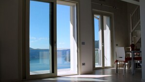 Une pièce spacieuse dotée de grandes portes-fenêtres coulissantes donnant sur un balcon avec vue sur la mer et les montagnes.