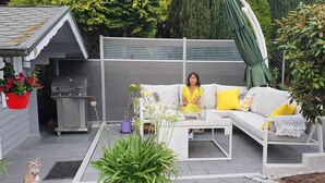 Eine Terrasse mit einer weißen Couch, einem Grill und Topfpflanzen.