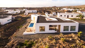 Une villa moderne aux murs blancs, dotée d’une piscine, et entourée d’un paysage rocheux ainsi que d’autres bâtiments blancs.