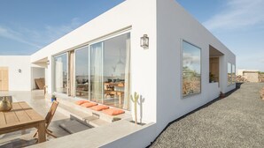Une maison moderne avec de grandes fenêtres en verre, un patio avec une table et des chaises, et un cactus.