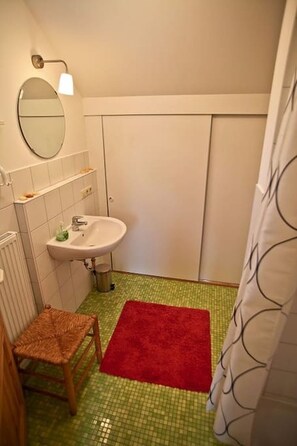 Un baño pequeño con un lavamanos blanco, un espejo y un tapete rojo en el suelo.