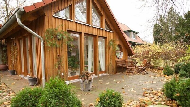 Een houten chalet met grote ramen, een terras en buiten zitplaatsen.