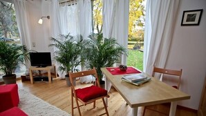 Een gezellige woonkamer met een houten tafel, stoelen, een televisie en potplanten.