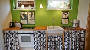 Een keuken met een groene wand, twee hanglampen, een witte spoelbak, een fornuis en een koffiezetapparaat.