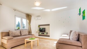 Ein modernes Wohnzimmer mit zwei Sofas, einem Couchtisch, einem Flachbildfernseher und einem Fenster mit Vorhängen.