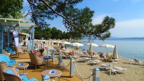 Ein Strandabschnitt mit Liegestühlen, Sonnenschirmen und einer überdachten Sitzgelegenheit.
