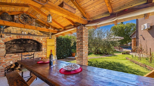 An outdoor patio with a brick oven, wooden table, and chairs. - Holiday house NOVKOVIC with garden (Žgaljići)