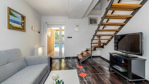 A modern living room with a grey sofa, a coffee table with a white vase, a flat-screen TV, and a wooden staircase. - Holiday house NOVKOVIC with garden (Žgaljići)