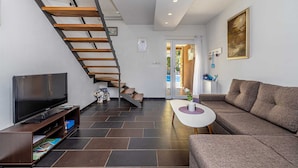 A modern living room with a wooden staircase, a flat-screen TV, a sofa, and a small table with a vase. - Holiday house NOVKOVIC with garden (Žgaljići)