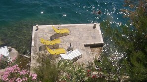 A rooftop terrace with yellow lounge chairs and a white chair, overlooking a body of water. - House directly by the sea (Klek)