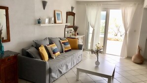 A living room with a grey sofa, a white coffee table, and a vase with flowers. There is a window with curtains and a view of the outdoors. - House directly by the sea (Klek)