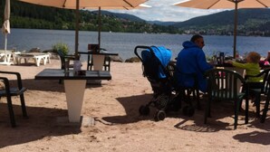 Zona de estar al aire libre con mesas y sombrillas con vista a un lago.