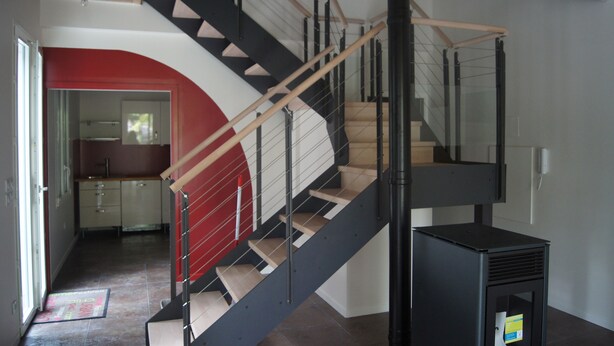 Una escalera moderna con barandillas de vidrio y peldaños de madera, que conduce a un piso superior.