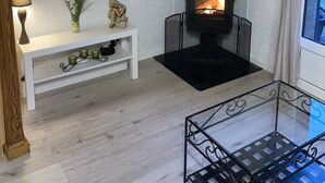 A cozy room with a fireplace, a TV mounted on the wall, a small white bench, and a glass table. - Duplex apartment 4/5 people at the foot of the slopes. Serre chevalier 1500 (Le Monêtier-Les-Bains)