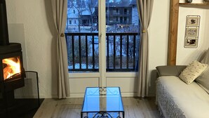 A cozy room with a fireplace, a glass table, a sofa, and a view of a snowy landscape through a large window. - Duplex apartment 4/5 people at the foot of the slopes. Serre chevalier 1500 (Le Monêtier-Les-Bains)