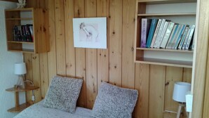 A bedroom with a wooden headboard, two fluffy pillows, a bedside table with a lamp, and a bookshelf filled with books. - Duplex apartment 4/5 people at the foot of the slopes. Serre chevalier 1500 (Le Monêtier-Les-Bains)