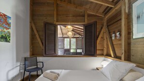 A bedroom with a wooden ceiling, a bed with white linens, a chair, and a window with shutters. - Villa Colibri - Three Bedroom Villa, Sleeps 6 (Le Vauclin)