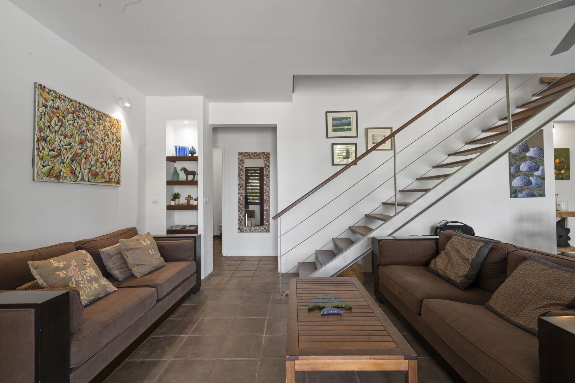 A living room with two sofas, a coffee table, a staircase, and a door leading to another room.