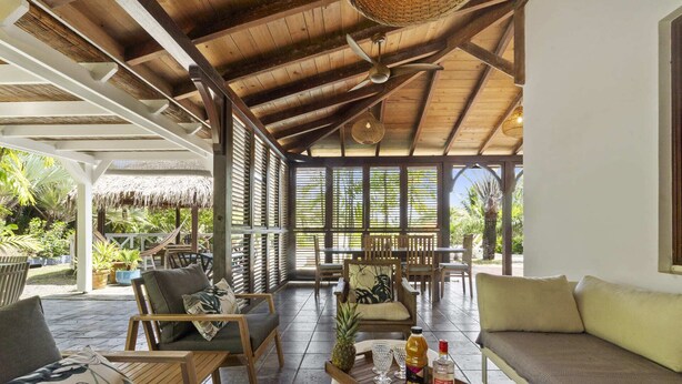 A covered outdoor seating area with wooden furniture, a thatched roof, and a view of tropical vegetation. - Villa Colibri - Three Bedroom Villa, Sleeps 6 (Le Vauclin)