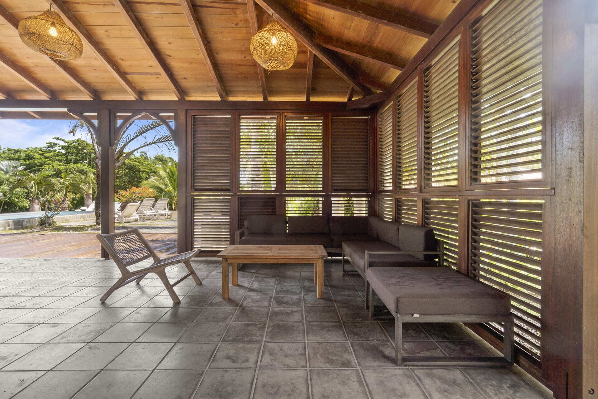 Un espace extérieur abrité, aménagé avec du mobilier en bois et offrant une vue sur la piscine.