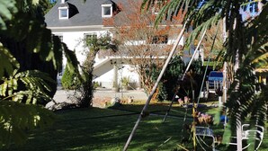 A residential property with a well-maintained lawn, a swing set, and a large house with a dark roof and multiple windows.