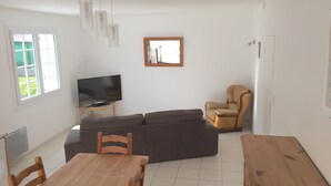 A living room with a TV, sofa, wooden dining table, and chairs.