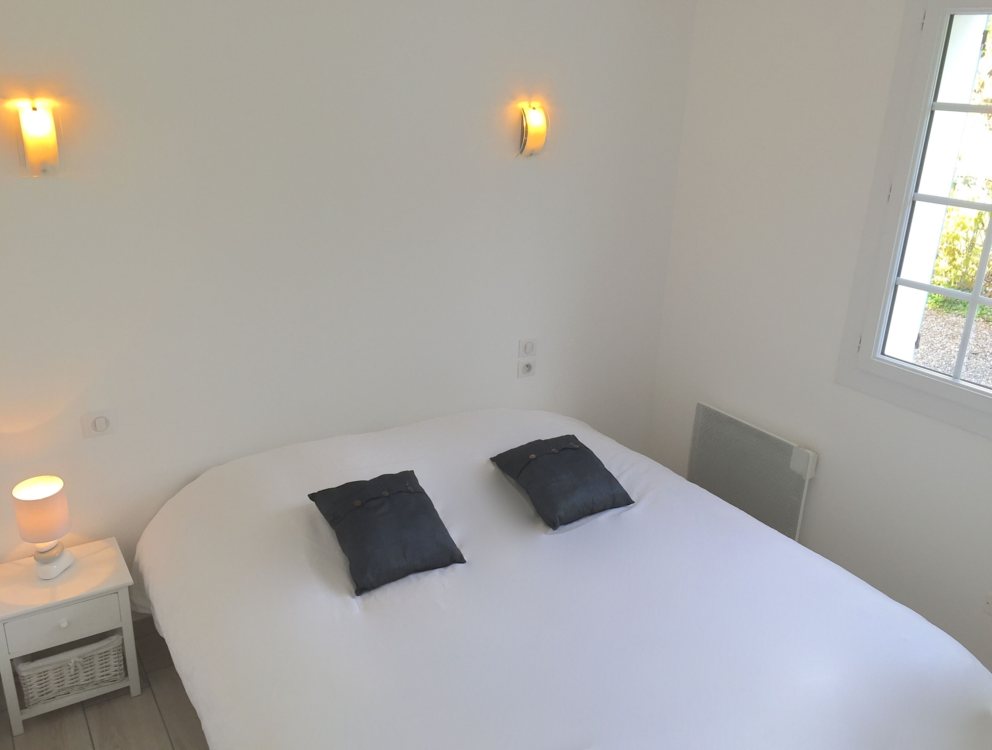 A bedroom with a bed, two pillows, a nightstand with a lamp, and two wall-mounted lights.