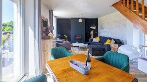 Ein modernes Wohnzimmer mit einem Holzespeisetisch, blaugrünen Stühlen, einem schwarzen Sofa und einer Treppe.