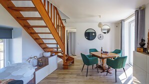 Ein modernes Interieur mit einer Holztreppe, einem Essbereich mit grünen Stühlen und einer Küche mit weißen Schränken.