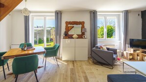 Ein modernes Wohnzimmer mit Essbereich, einer Couch, einem Fernseher und einem großen Fenster mit Blick ins Freie.