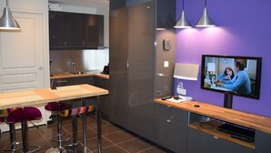 A modern kitchen with a dining area, a TV, and a purple accent wall.
