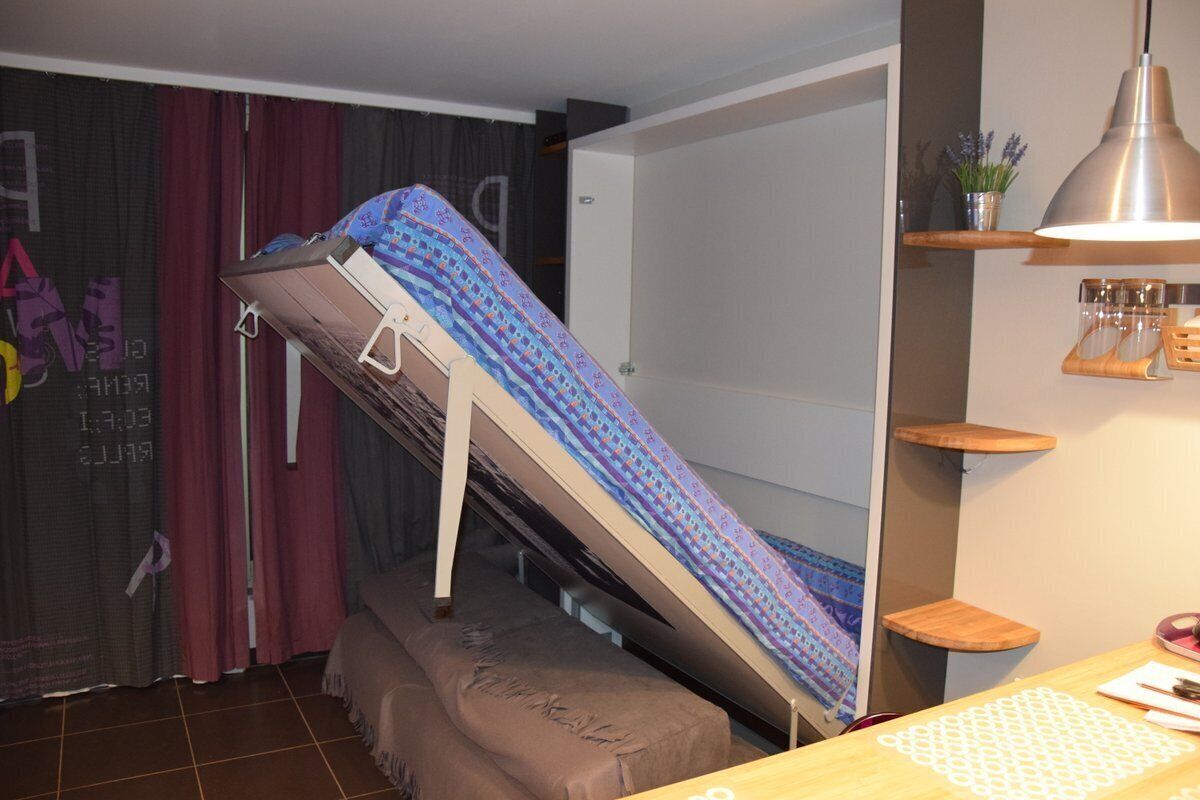 A bunk bed with a blue patterned bedspread, a bedside table with a lamp, and a shelf with glasses and a plant.