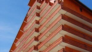 A multi-story building with balconies, a wooden facade, and a clear sky.
