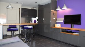 A modern kitchen with a bar area, a flat-screen TV, and a purple accent wall.