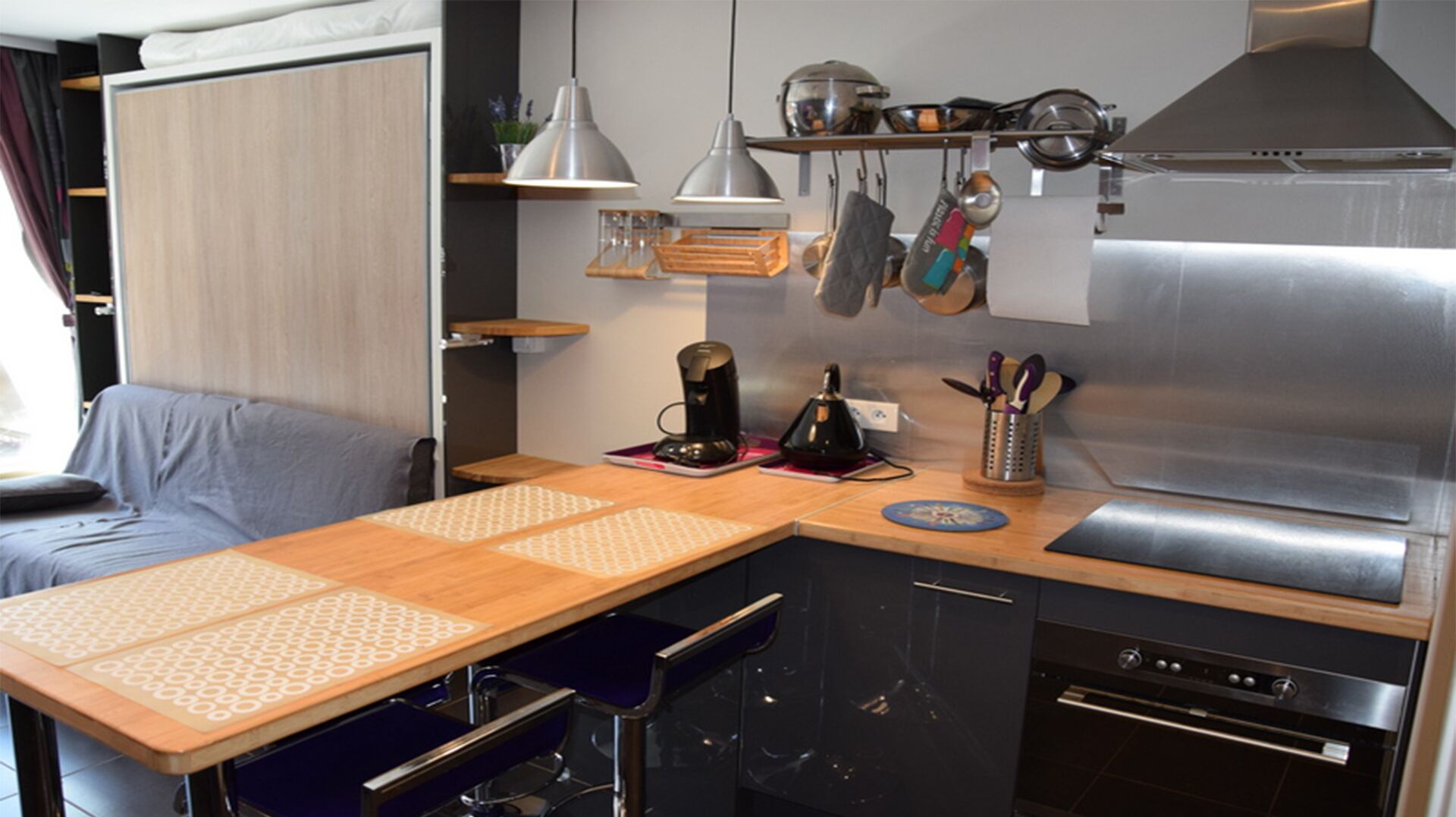 Una kitchenette compacta con cafetera, hervidor y utensilios en la encimera.