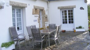 Un edificio bianco con dettagli in pietra, un patio in pietra, un tavolo con sedie e un cartello con su scritto "TANKADI".