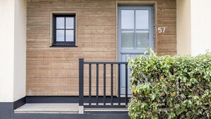 Une façade d’immeuble avec un revêtement extérieur en bois, une petite fenêtre, une porte et le numéro « 57 » peint sur le mur.