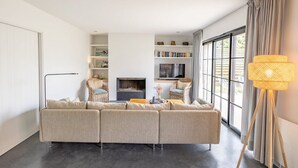 Un salon moderne avec un canapé d’angle, une cheminée, des étagères et une grande fenêtre avec des rideaux.
